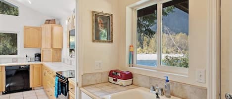 A kitchen with wooden cabinets, a dishwasher, and a window with a view of trees.