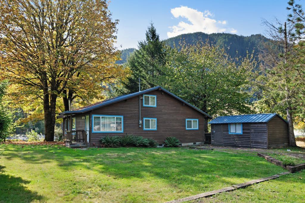 Eine zweistöckige Holzhütte mit Veranda, umgeben von einem gepflegten Rasen und Bäumen.