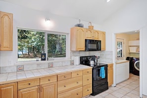 A kitchen with wooden cabinets, a microwave, a stove, and a window with a view of trees.