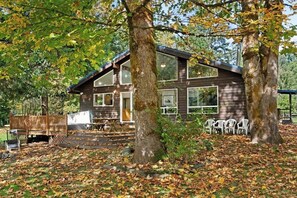 A cabin with a deck, surrounded by trees and covered in fallen leaves.