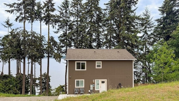 A two-story building with a brown exterior, a flat roof, and a small front porch with two chairs. - 3BR Bayview | Hot Tub | Deck | Firepit (Port Hadlock)