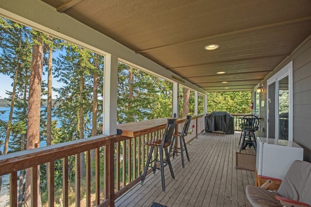 Une terrasse couverte avec une rambarde en bois, des tabourets de bar, un barbecue et une table.