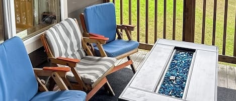 A deck with a fire pit table, two lounge chairs, and a view of a grassy yard.
