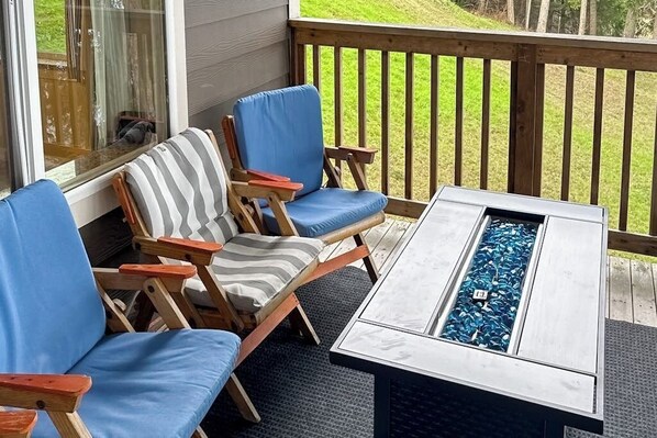 A deck with a fire pit table, two lounge chairs, and a view of a grassy yard.