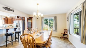 A dining area with a wooden table and chairs, a chandelier, and a view of the outdoors through a window. - 3BR Bayview | Hot Tub | Deck | Firepit (Port Hadlock)