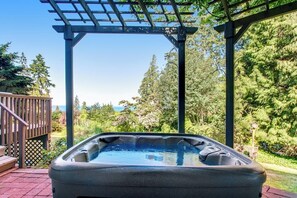 Ein Whirlpool unter einer Pergola mit Blick auf einen Garten und Bäume.