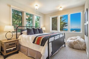 A bedroom with a bed, two bedside lamps, a window with a view, and a fluffy ottoman. - Stunning 5BR Oceanview Birch Bay Dog Friendly (Blaine)