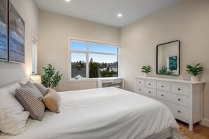 A bedroom with a large bed, a desk, and a dresser. There is a window providing a view of the outside. - 1BR All-New - Central AC - Full Kitchen (Seattle)