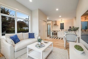 A modern living space with a sofa, coffee table, and a view of a kitchen area. - 1BR All-New - Central AC - Full Kitchen (Seattle)