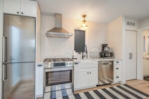 Una cucina moderna con elettrodomestici in acciaio inossidabile, mobili bianchi e un tappeto a righe bianche e nere.