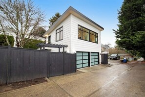 A modern two-story house with a garage, a fenced driveway, and a clear sky. - 1BR All-New - Central AC - Full Kitchen (Seattle)