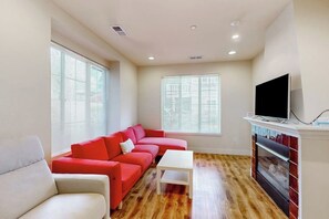 A living room with a red sectional sofa, a white armchair, a small white table, a fireplace, and a television. - Bright 2BR with deck, office & central location (Redmond)