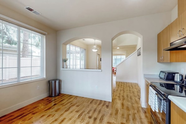 A modern kitchen with wooden flooring, a built-in oven, and a window with blinds. - Bright 2BR with deck, office & central location (Redmond)