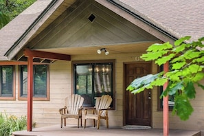 Ein Holzhaus mit Veranda, zwei Stühlen und einer Tür.