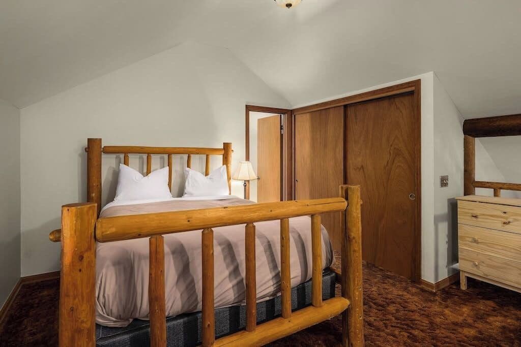 Quarto com cama de madeira, penteadeira e porta.
