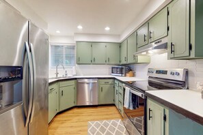 Une cuisine moderne dotée d’appareils électroménagers en acier inoxydable, de meubles de couleur verte et d’un plancher en bois.
