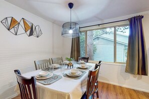 A dining area with a table set for four, chairs, a hanging light fixture, and a window with curtains. - Downtown 3BR Dog Friendly - Fireplace - Washer Dryer (Bellingham)