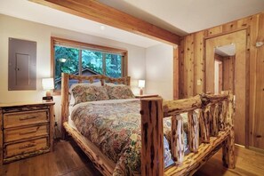 Ein Schlafzimmer mit einem hölzernen Bettgestell, einem Nachttisch und einem Fenster mit Blick auf Bäume.