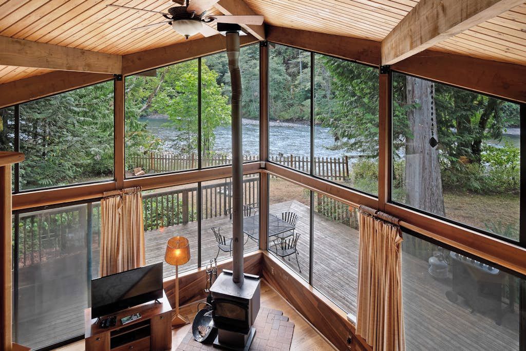 A cabin with a large window overlooking a forest and a river.