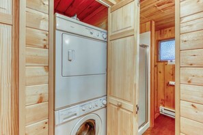 Ein kleiner Hauswirtschaftsraum mit einer Frontlader-Waschmaschine und einem Trockner, Holzwänden und einem kleinen Fenster.