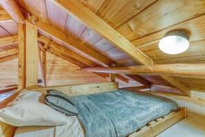 Een houten interieur met een bed, kussens en een plafondlamp.