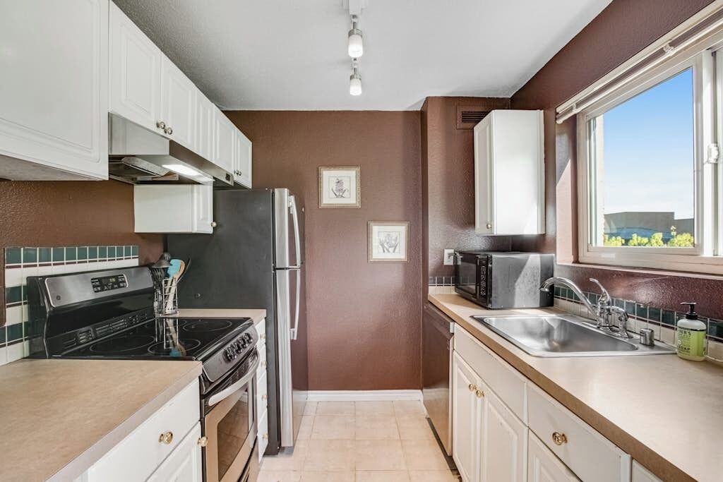 A compact kitchen with white cabinets, a black refrigerator, a microwave, and a stainless steel sink.