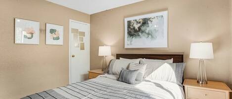 A bedroom with a bed, two bedside tables with lamps, a ceiling fan, and three framed artworks on the wall.