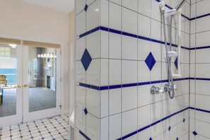 Ein Badezimmer mit weißen Fliesen und blauen Akzenten, eine Duschkabine und eine Tür zu einem Zimmer mit Blick.