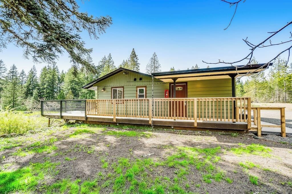 A cabin with a wooden deck, a covered porch, and a view of a forested area.