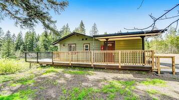 A cabin with a wooden deck, a covered porch, and a view of a forested area.