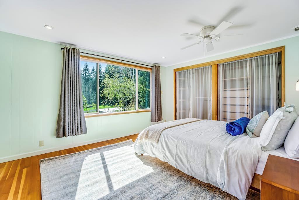 Un dormitorio con cama, ventilador de techo y un ventanal con cortinas.