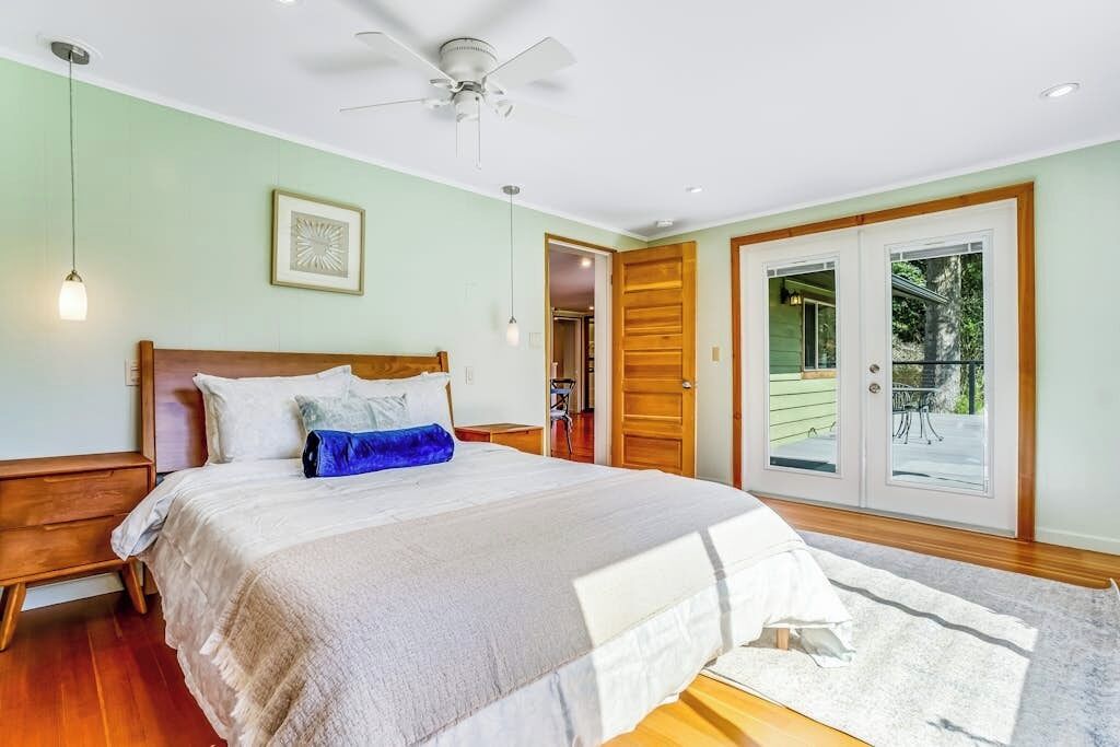 Un dormitorio con una cama, ventilador de techo, puerta que da a un balcón, y una lámpara.