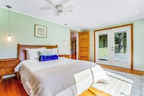 Une chambre à coucher comprenant un lit, un ventilateur de plafond, une porte donnant sur un balcon et un luminaire.