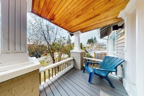 A covered porch with a wooden ceiling, a white railing, and a blue Adirondack chair. - Woodland 1BR - Patio - Washer Dryer (Seattle)