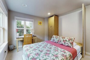 Een slaapkamer met een bed, een bureau, een stoel, een kledingkast en een raam met uitzicht op groen.