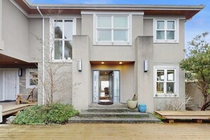 Een tweelaags huis met een veranda, een houten terras en een kleine tuin.