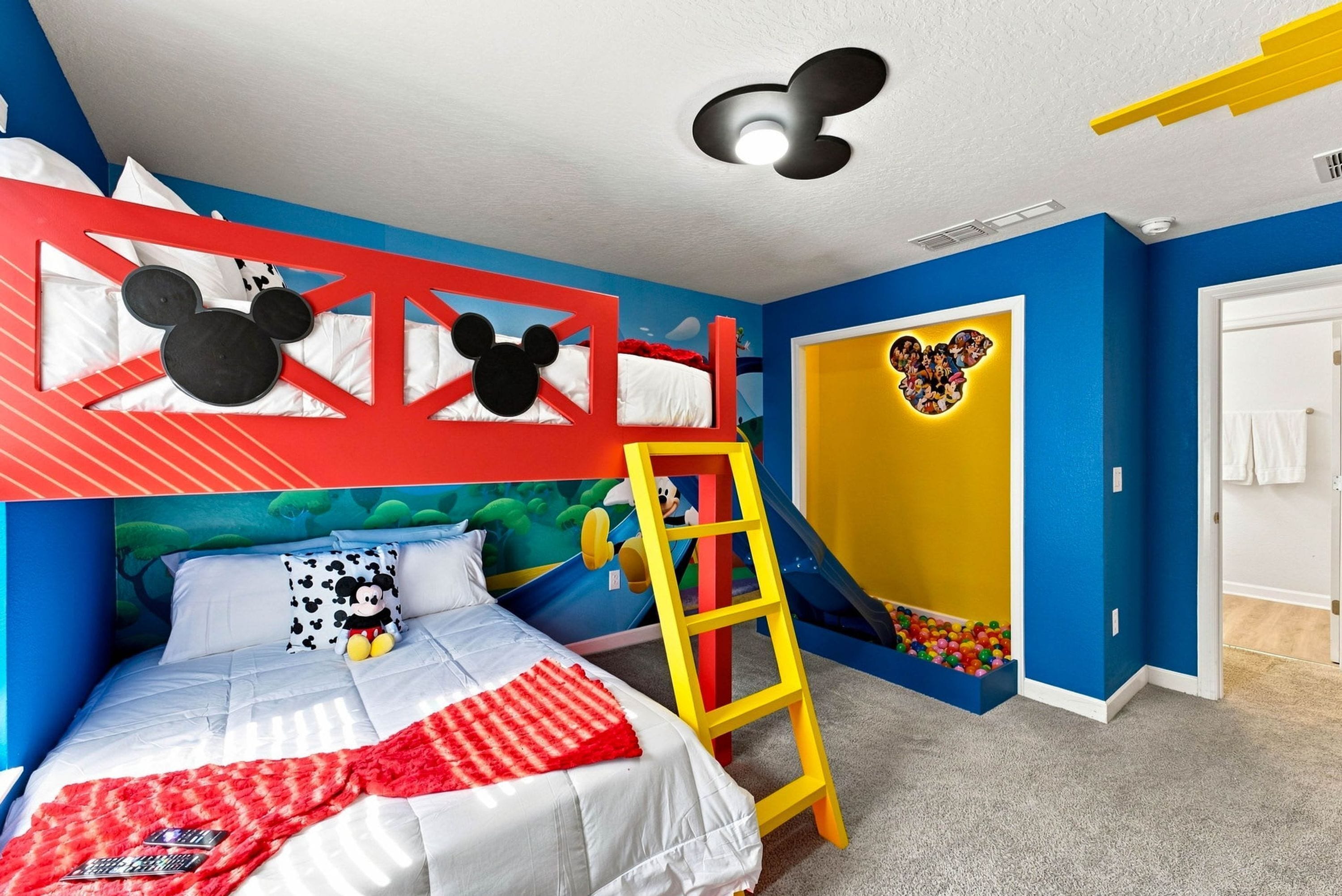A child's bedroom with a bunk bed, a ladder, a Mickey Mouse headboard, a wall mural, and a door with a cartoon character.