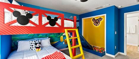 A child's bedroom with a bunk bed, a ladder, a Mickey Mouse headboard, a wall mural, and a door with a cartoon character.