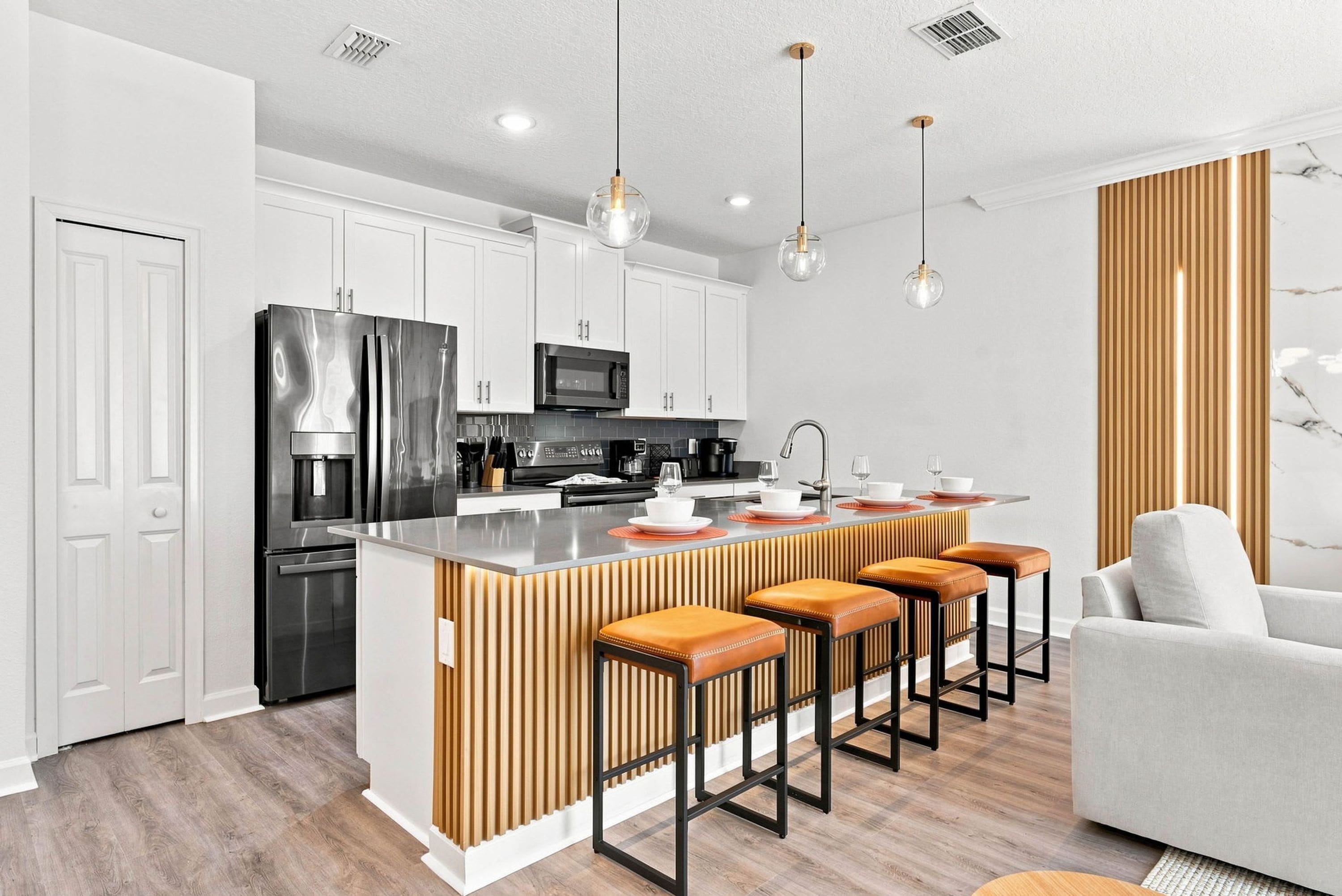 Cocina moderna con isla central, taburetes de bar y zona de comedor con sofá blanco.