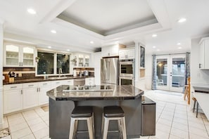 A modern kitchen with a central island, bar stools, and built-in appliances. - 5BR Oceanview - Hot Tub - Fireplace - Balcony (Camano Island)