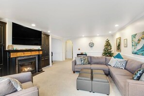 A living room with a fireplace, a large flat-screen TV, a sectional sofa, and a Christmas tree. - 5BR Oceanview - Hot Tub - Fireplace - Balcony (Camano Island)