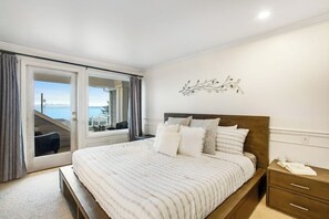 A bedroom with a large bed, a nightstand, a wall-mounted decoration, and a view through a sliding door. - 5BR Oceanview - Hot Tub - Fireplace - Balcony (Camano Island)
