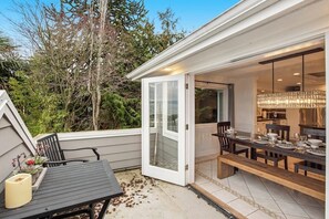 An outdoor dining area with a table and chairs, a bench, and a glass door leading to an interior space with a dining table set. - 5BR Oceanview - Hot Tub - Fireplace - Balcony (Camano Island)