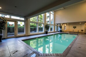 An indoor swimming pool with a clear view of the surrounding buildings and greenery. - 1BR 5th-floor studio withheated pool, gym, hot tub (Seattle)