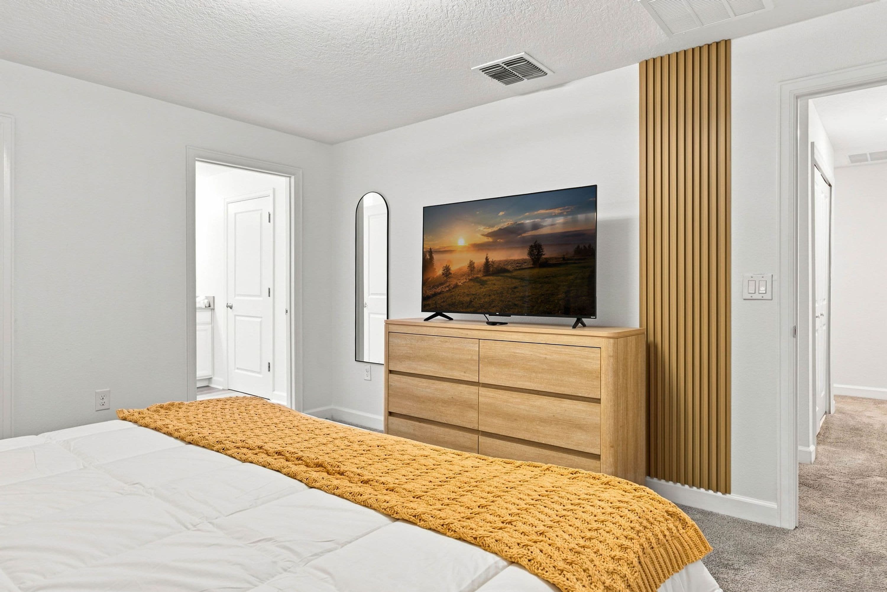 A bedroom with a bed, a TV on a wooden dresser, a mirror, and a door.