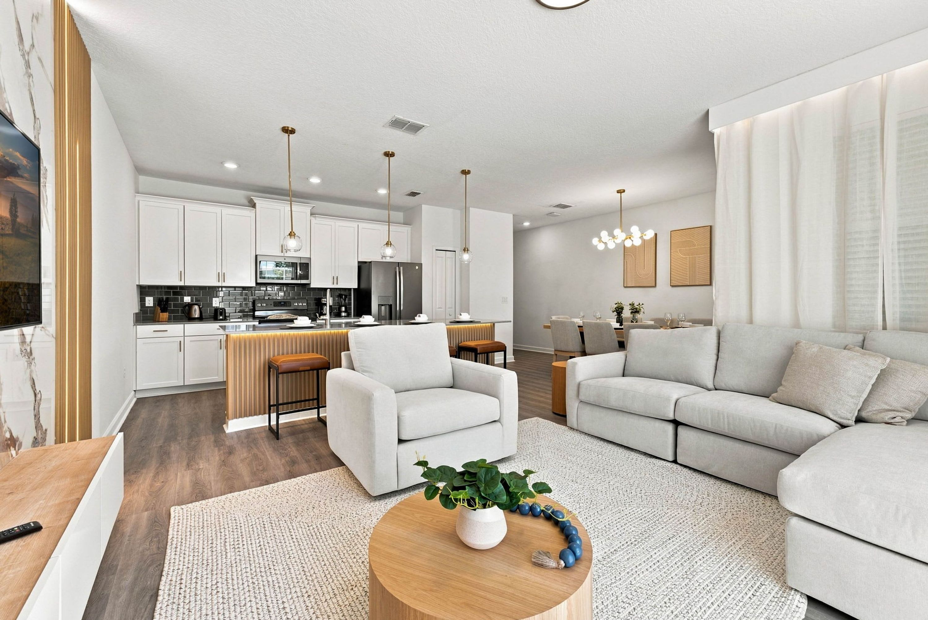 A modern living room with a sofa, a coffee table with a plant, and a kitchen area with cabinets and appliances.