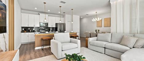 A modern living room with a sofa, a coffee table with a plant, and a kitchen area with cabinets and appliances.