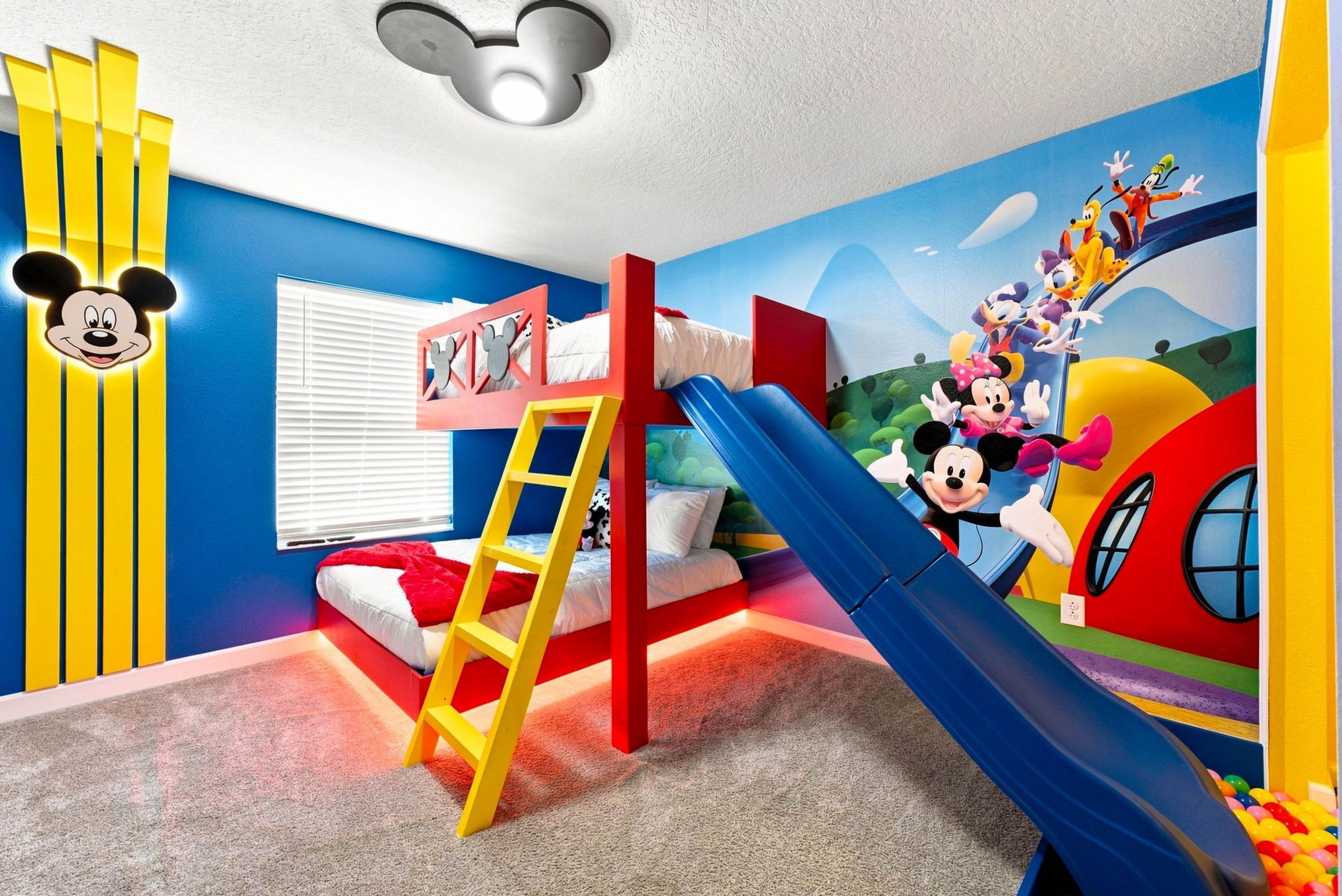 A children's room with a bunk bed, a slide, and a Mickey Mouse wall decal.