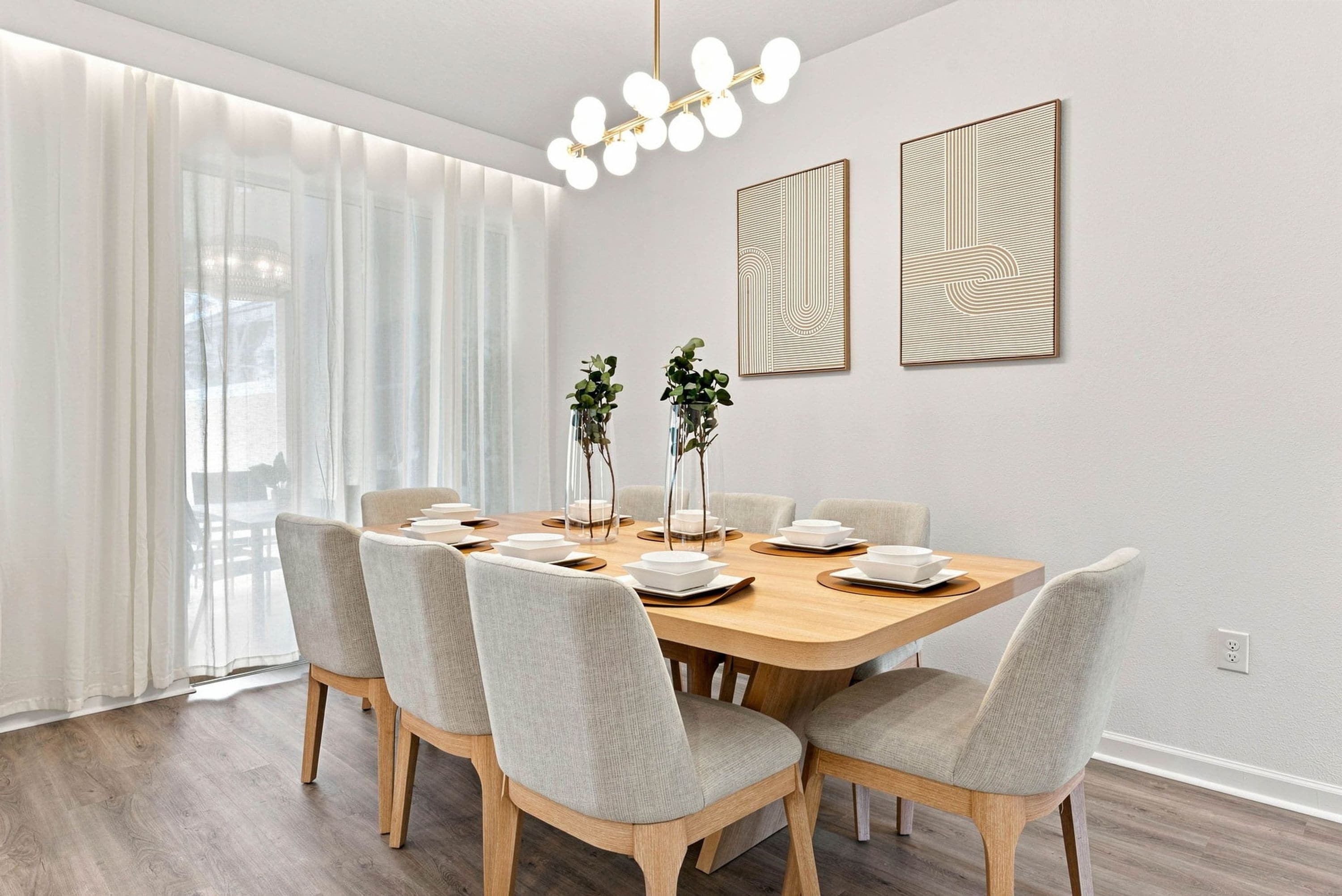 A dining area with a wooden table, six chairs, and two vases with plants.