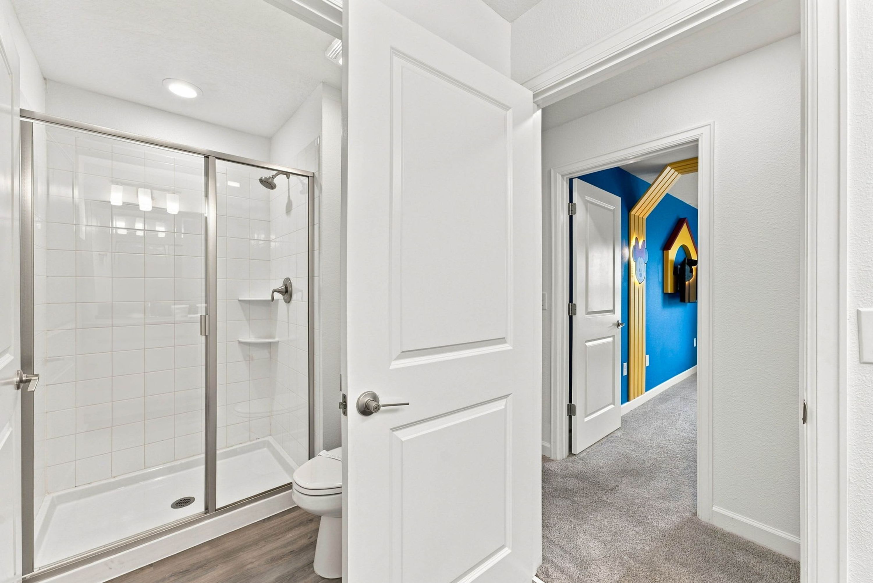 Un baño moderno con cabina de ducha de vidrio, un inodoro y una puerta blanca que da a un pasillo.